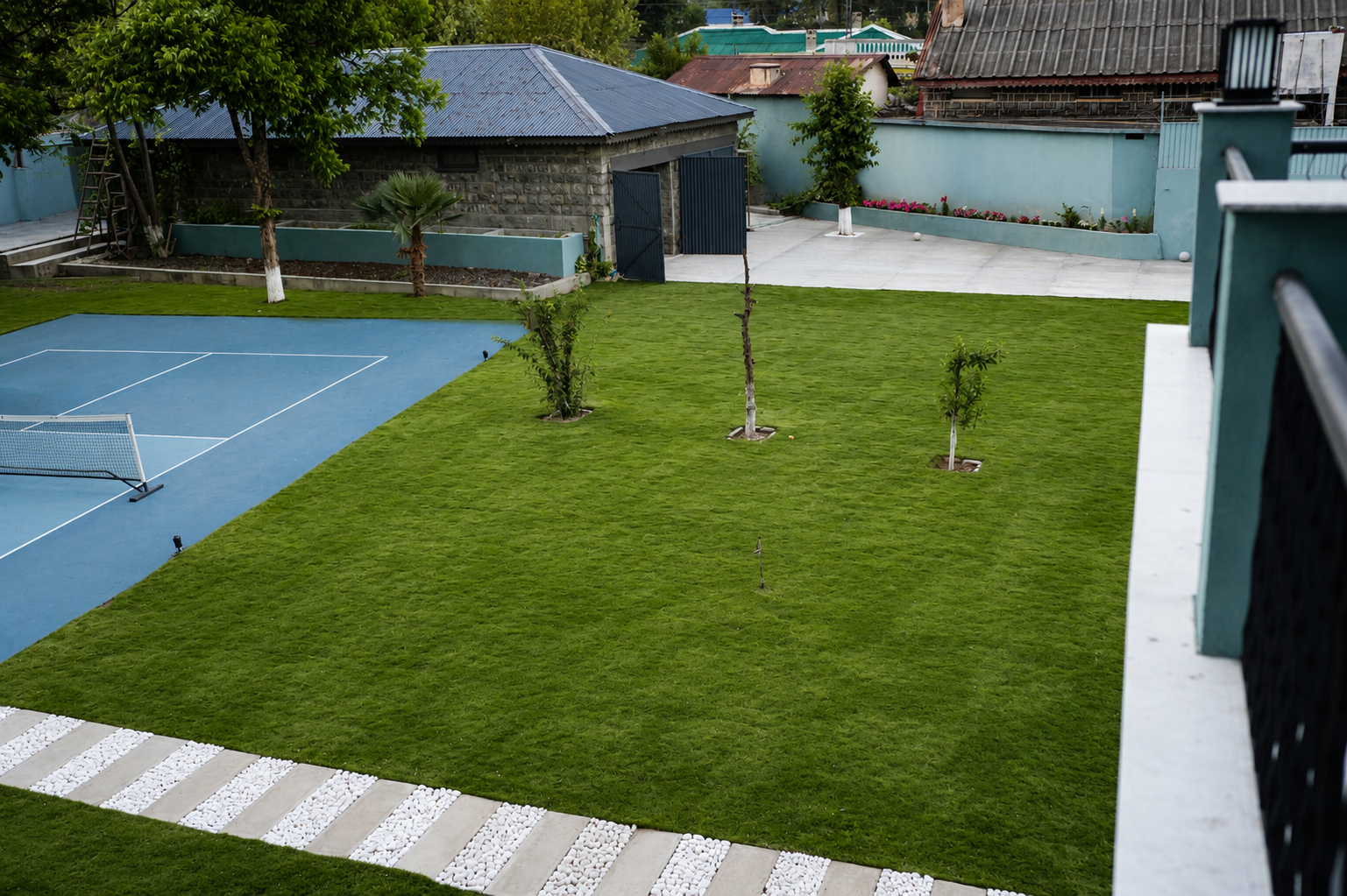 Aerial view of Jhangi House grounds — pickleball court, lawn, pebble paths, and pavilion